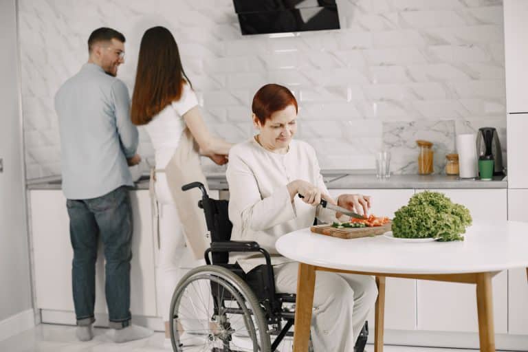 Femme âgée en fauteuil roulant cuisinant dans la cuisine. représentation de personnes en situation de handicap. Un couple l'aidant.